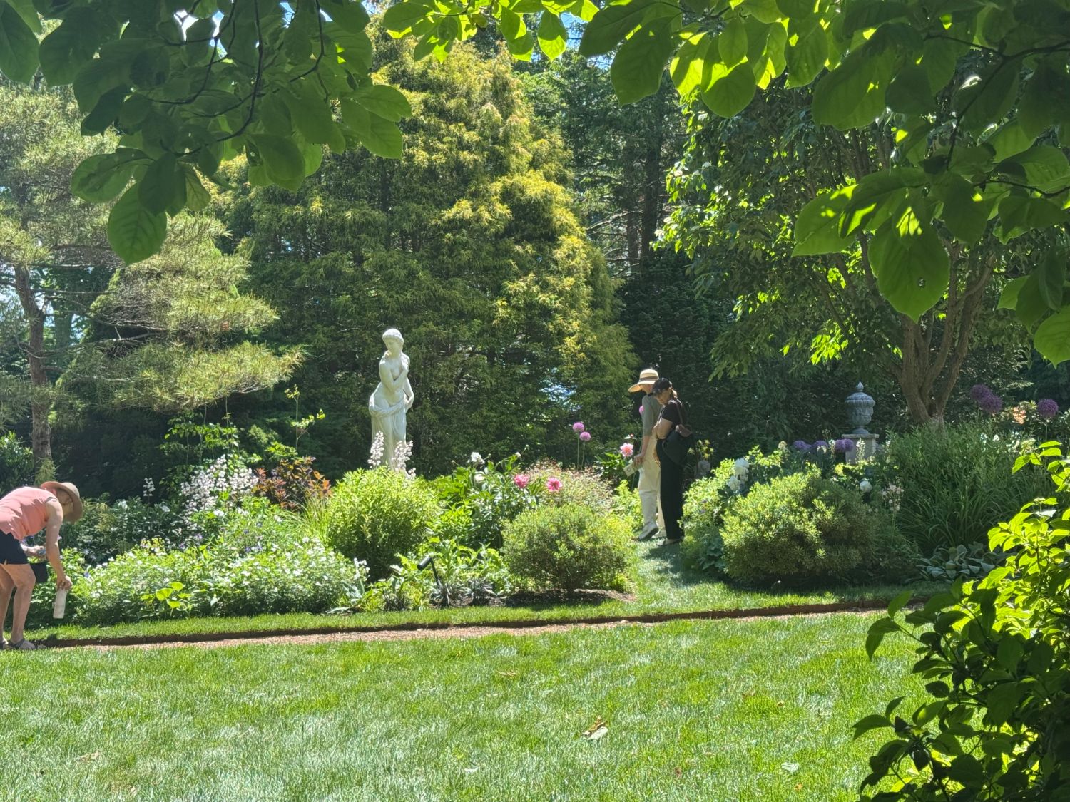 Visitors walking the garden paths past a classical statue and mixed plantings at Sleepy Cat Farm
