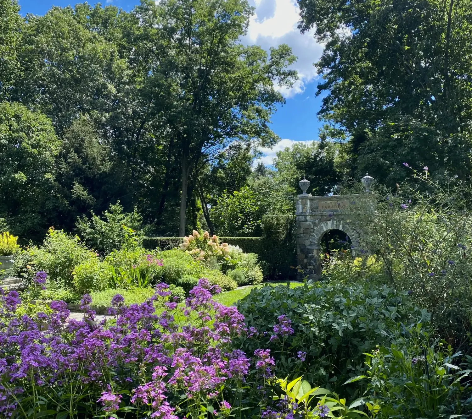 Sleepy Cat Farm — perennial borders in bloom leading to the stone Paradiso arch, Greenwich, Connecticut
